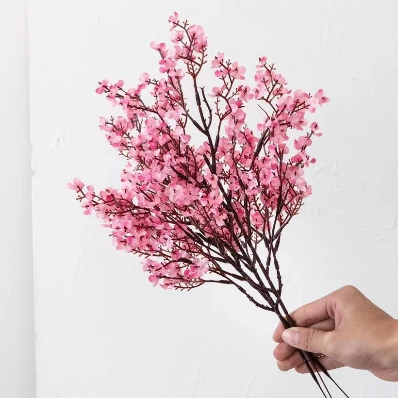 Multicolor artificial sakura flowers bouquet held in hand against a neutral background.