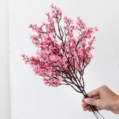 Multicolor artificial sakura flowers bouquet held in hand against a neutral background.