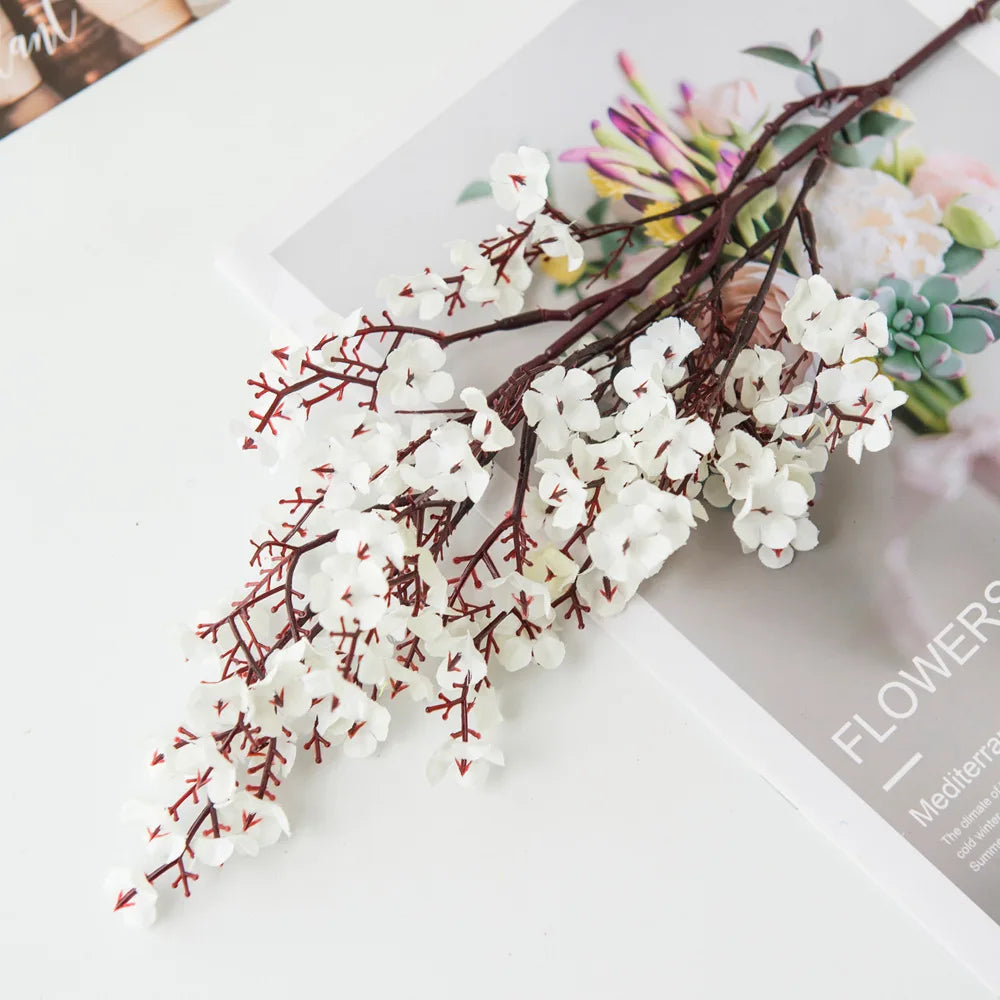 Multicolor artificial sakura flowers arrangement on a table with floral magazine.