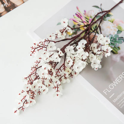 Multicolor artificial sakura flowers arrangement on a table with floral magazine.