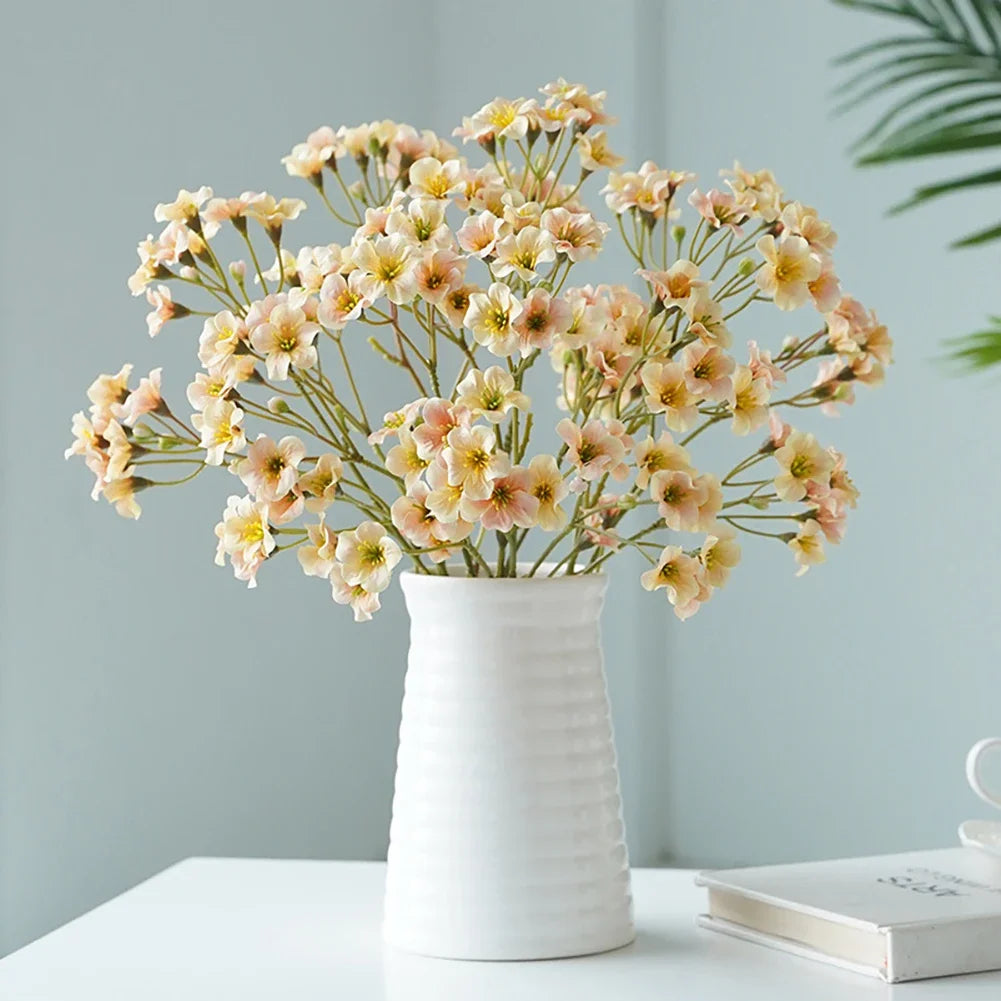 Artificial cornflower decorative flowers arranged in a white vase on a table.