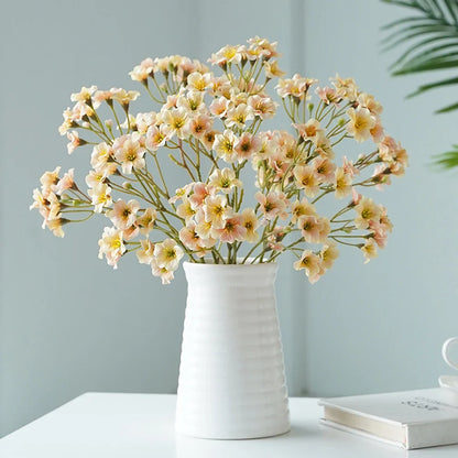 Artificial cornflower decorative flowers arranged in a white vase on a table.