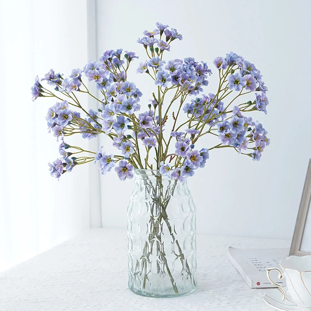 Artificial cornflower decorative flowers arranged in a glass vase on a table.