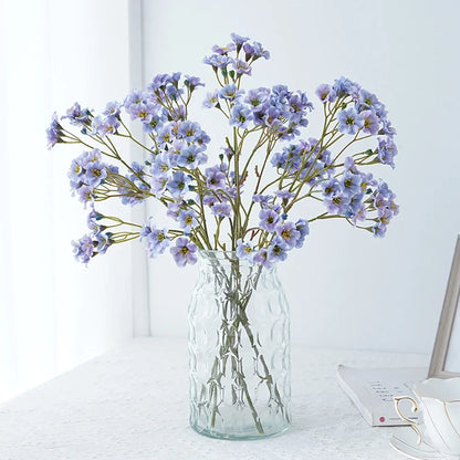 Artificial cornflower decorative flowers arranged in a glass vase on a table.